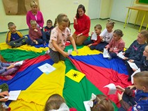 Dzieci siedzą w kole na kolorowej chuście i przyporządkowują obrazki
