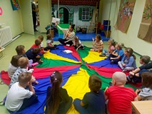 Dzieci siedzą na kolorowej chuście animacyjnej i słuchają opowiadania