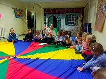 Dzieci siedzą w kole na kolorowej chuście, podczas zabawy integracyjnej