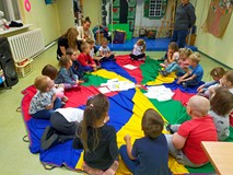 Dzieci siedzą w kole na kolorowej chuście i przyporządkowują obrazki