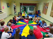 Dzieci siedzą w kole na kolorowej chuście i przyporządkowują obrazki