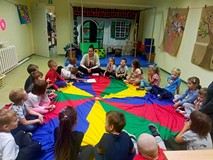 Dzieci siedzą na kolorowej chuście animacyjnej i rozmawiają o skarbach jesieni