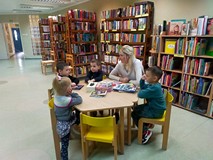 Dzieci wraz z bibliotekarką siedzą przy stoliku