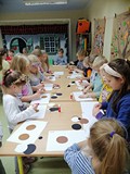 Dziecie stoją przy stołach i wykonują prace plastyczną