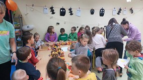 Dzieci stoją przy stolikach i wykonują prace plastyczną