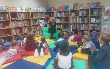 Dzieci słuchają opowiadania, które czyta im bibliotekarka