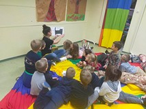 Dzieci siedzą na materacach i słuchają opowiadania