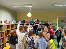 Bibliotekarka zdejmuje zawieszony balon z zagadką, a przedszkolaki czekają w kole