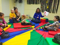 Bibliotekarka czyta książkę, dzieci siedzą na kolorowej chuście animacyjnej