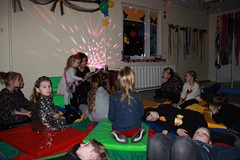 Bibliotekarka czyta książkę, dzieci siedzą na chuści i słuchaja opowiadania