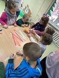 Dzieci stoją przy stolikach i wykonują prace plastyczne