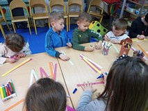 Dzieci stoją przy stolikach i wykonują prace plastyczne