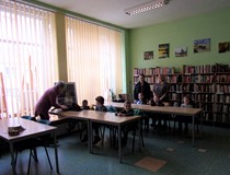 na zdjęciu dzieci słuchają co mówi bibliotekarka