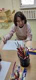 Uczestnicy zajęć siedzą na krzesełkach i słuchają opowiadania czytanego przez bibliotekarkę
