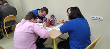 Uczestnicy WTZ siedzą przy stolikach i wykonują prace plastyczną