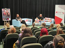 Na scenie siedzą Wojciech Chmielarz i prowadzący spotkanie Piotr Pawłowski