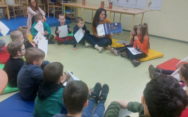Dzieci podczas zajęć siedzą w kole na kolorowych materacach i słuchają opowiadania,...