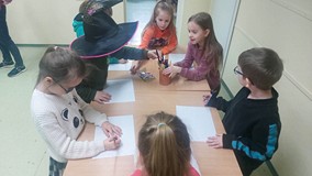 Dzieci stoją przy stolikach i wykonuja prace plastyczną