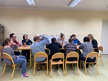 Bibliotekarka wraz  z uczestnikami zajęć siedzą przy wspólnym stole i rozmawiają o przeczytanej ksia