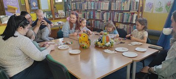 dzieci z rodzicami siedzą przy stole i wykonują pracę plastyczną