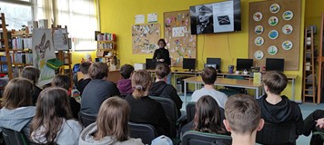 mlodzież siedzi na krzesłach, podczas gdy Pani Soraya Kuklińska opowiada o Powstaniu Warszawkim