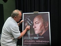 Janusz L. Wiśniewski podpisuje plakat wydarzenia.