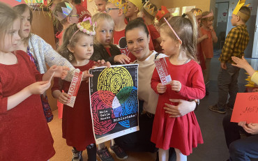 Bibliotekarka z dziećmi prezentuje plakat promujący Tydzień Bibliotek