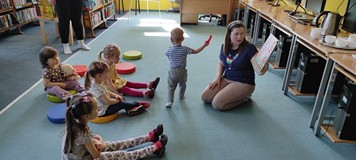 bibliotekarka czyta książkę dzieciom siedzącym na pufkach