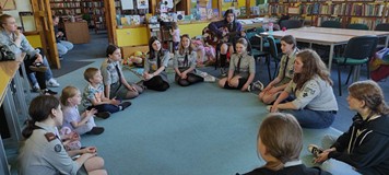 harcerka gra na gitarze dzieciom siedzącym na dywanie