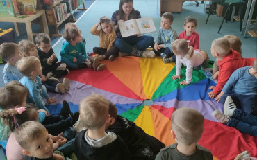 bibliotekarka pokazuje dzieciom siedzącym na chuście amimacyjnej