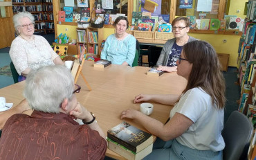 uczestniczki dkk wraz z bibliotekarką siedzą przy stole i dyskutują o książce