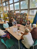uczestniczki dkk wraz z bibliotekarką siedzą przy stole i dyskutują o książce