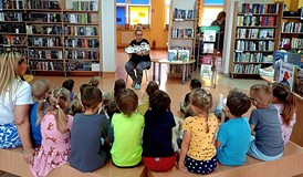 Na zdjęciu przedszkolaki siedzą na podłodze i słuchają Gosi czytającej 