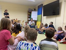 Bibliotekarka czyta dzieciom wiersz. Dzieci siedzą na materacykach