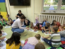 Dzieci siedzą na materacykach i uzupełniają rysunki, zgodnie ze wskazówkami bibliotekarki