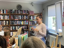 Bibliotekarka pokazuje dzieciom kartę biblioteczną, a dzieci stoją przed biurkiem