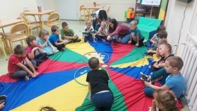 Dzieci podczas zabawy integracyjnej, siedzą na chuście animacyjnej i przyporządkowują dary jesieni