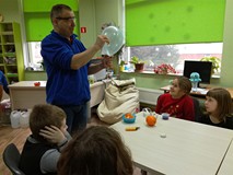 Prowadzący pokazuje, jak  przedziurawić balon skórką z pomarańczy