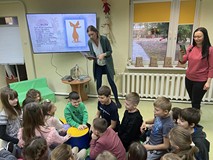 Dzieci siedzą na materacykach słuchając opowieści bibliotekarki