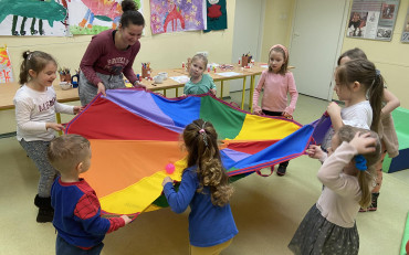 Dzieci z bibliotekarką podczas zabawy z kolorową chustą animacyjną