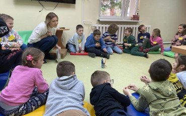 Uczniowie siedzą w kole wraz z bibliotekarką i rozmawiają