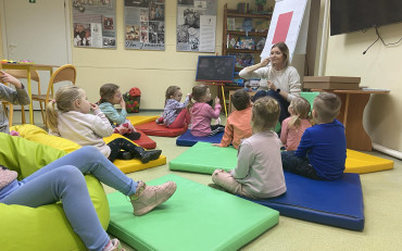 Dzieci siedxą na materacykach i słuchają bibliotekarki