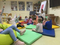 Dzieci siedxą na materacykach isłuchają bibliotekarki