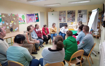 Uczestnovy siedzą w kole i sluchają opowiadania czytanego przez bibliotekarkę