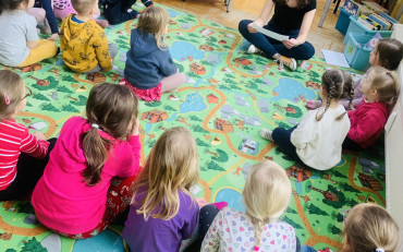 Dzieci siedzą na dywanie i bibliotekarka czyta list od Pani Wiosny