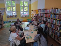 Bibliotekarka wraz z uczestniczkami DKK siedzi przy stole i dyskutuje na temat książki W. Chmielarza