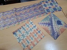 Na stole leżą kawałki tkaniny zafarbowane w unikalne wzory przez jedną z Pań