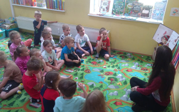 Bibliotekarka czyta dzieciom księżeczkę, dzieci siedzą w kole