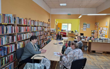 Panie wraz z bibliotekarką siedzą przy stole i dyskusują na temat książki