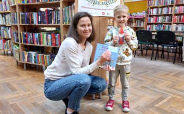 Chłopiec z bibliotekarką pokazują książkę i zakładkę